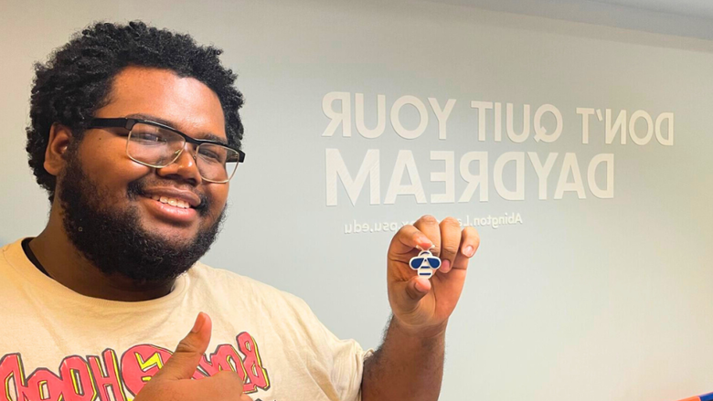 Darryl Gregory holds up a 3D print of a bee in front of a wall that says "Don't quit your daydream."